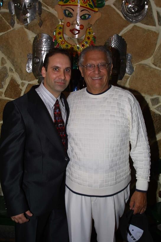 Two men smile and pose together at a vibrant gathering adorned with colorful decor.