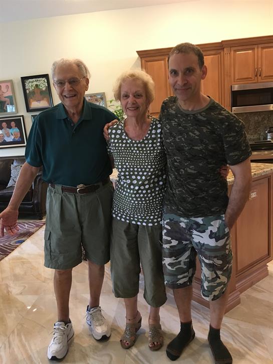 Three individuals share smiles in a warm kitchen, celebrating togetherness during a family visit.
