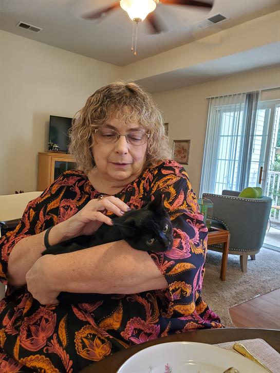 A woman holds her black cat closely while sitting in a comfortable living room, relaxing.