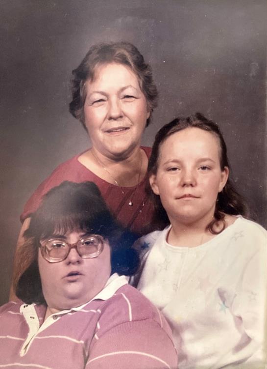 Three women share a warm moment, showcasing generational bonds against a studio backdrop.