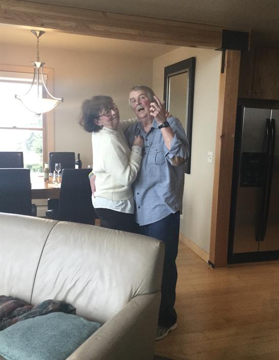 An elderly couple shares a playful dance in their home, surrounded by warmth and laughter.