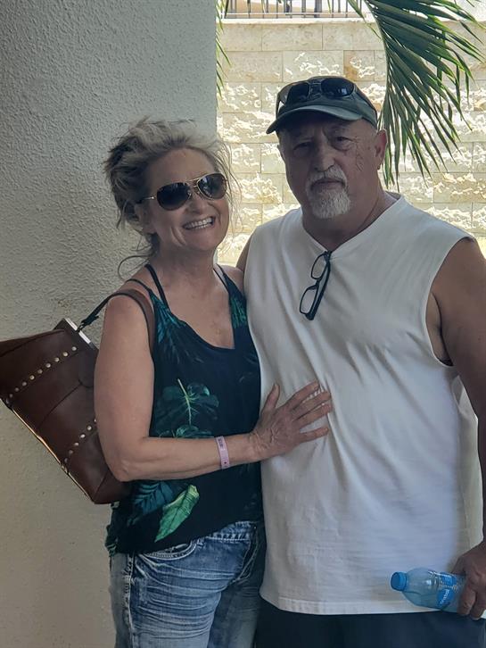 Happy couple poses together at a tropical location with palm trees and sunshine.