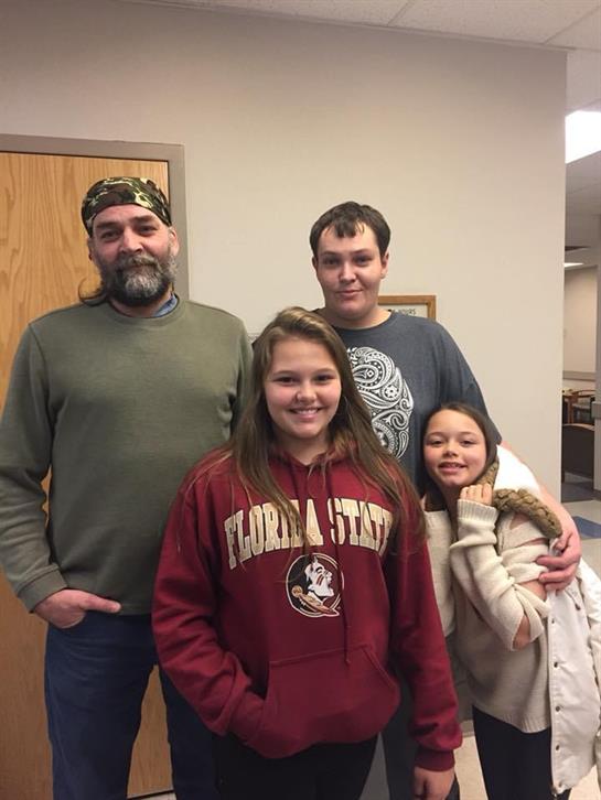 Group of four people pose together in a hallway. They smile and show a sense of togetherness.