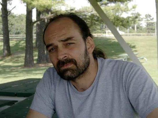 A man sits on a bench in a park, deep in thought as he watches the trees around him.