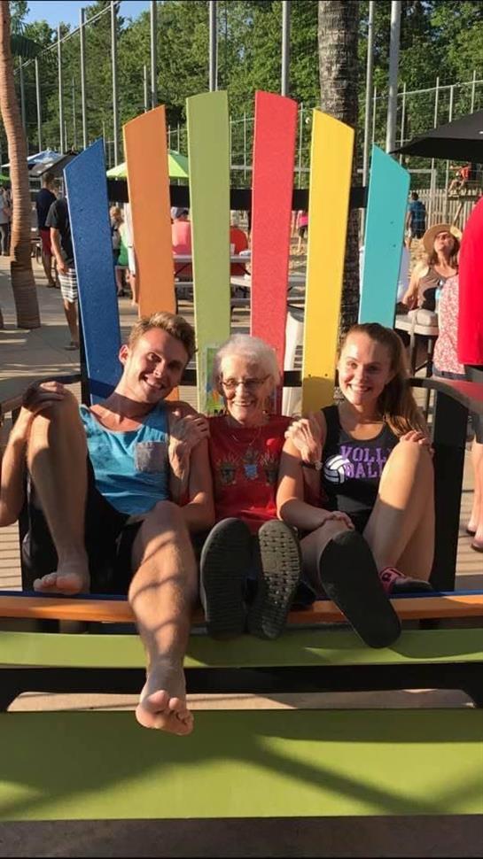 Family members share a colorful oversized chair in a vibrant park during a sunny day.