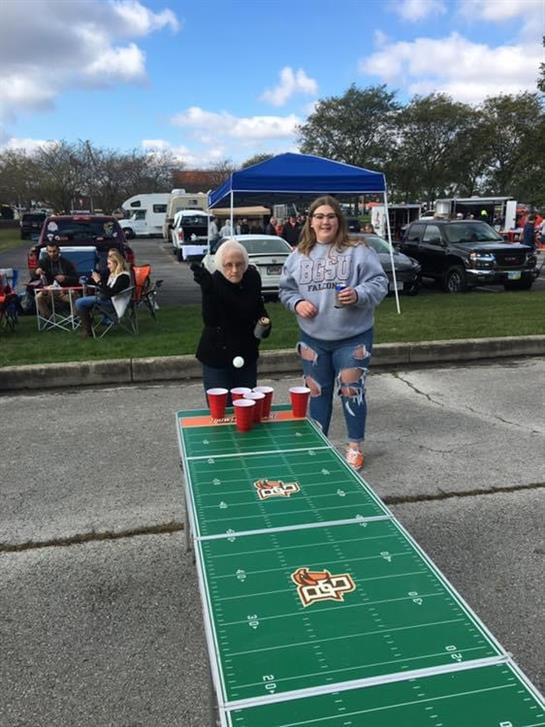 Friends enjoy a lively game of beer pong while tailgating at a sports event with food and drinks.