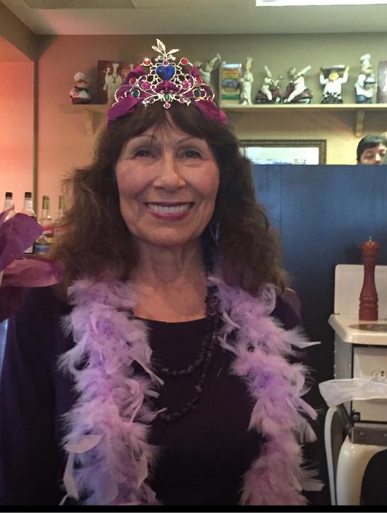 A woman smiles joyfully while wearing a tiara and feather boa during a festive gathering.