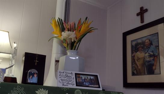 Brightly colored flowers are arranged in a vase on a shelf adorned with photographs and decor.