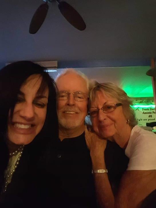 Three friends smile and embrace each other in a warm and inviting indoor space at night.