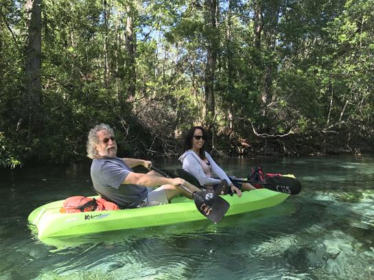 Two paddlers enjoy a peaceful kayak ride in clear water surrounded by lush trees.