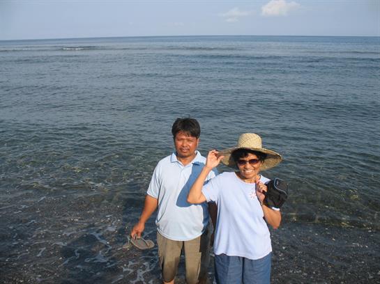 A man and woman stand in shallow water, both smiling and enjoying their day at the beach.