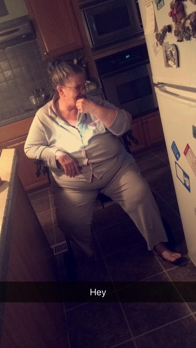 A woman in comfy pajamas sits in her kitchen, thoughtfully gazing at the refrigerator.