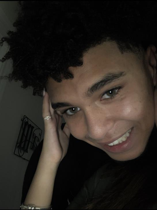 A young person smiles warmly, leaning on their hand in a joyful moment.