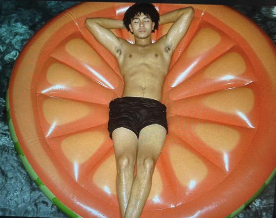 Calm moment of a young individual lounging on an orange slice float in clear water.