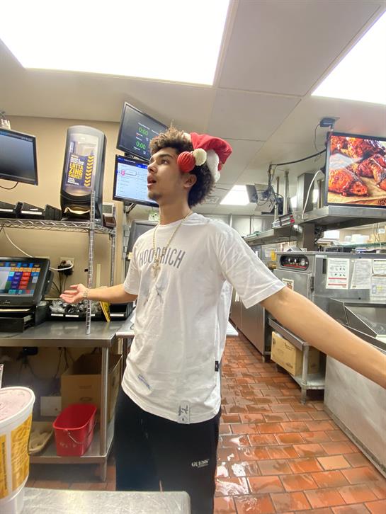 A young worker in a Santa hat joyfully engages in a busy holiday kitchen.
