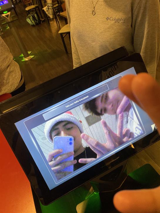 Two friends pose for a selfie using a tablet while enjoying their time together indoors.