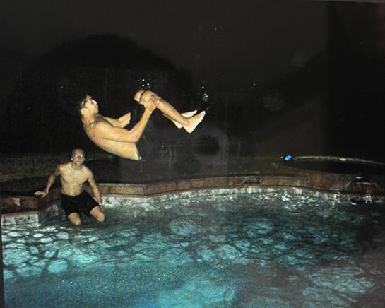 A young man backflips into a glowing pool while another man watches and enjoys.