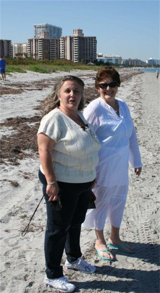 Two women stand together on a sandy beach, enjoying a warm day and the ocean breeze.