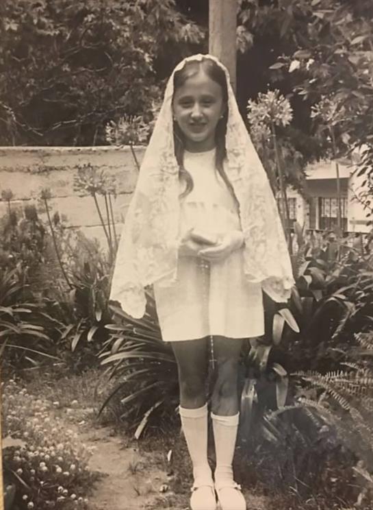 A girl in a white dress with a lace veil holds a bouquet in a lush garden setting.