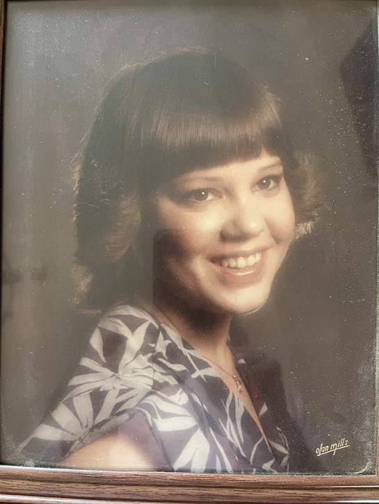 A young woman smiles in a floral dress, flaunting a retro hairstyle.