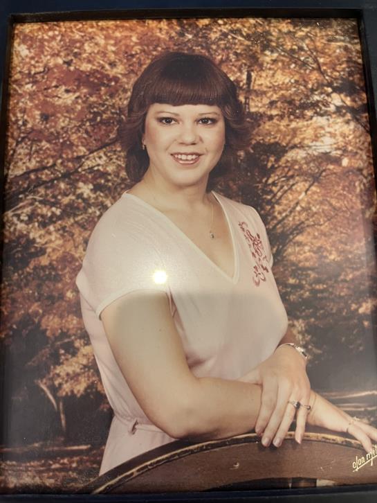 A woman stands confidently with a warm smile in front of colorful autumn leaves.