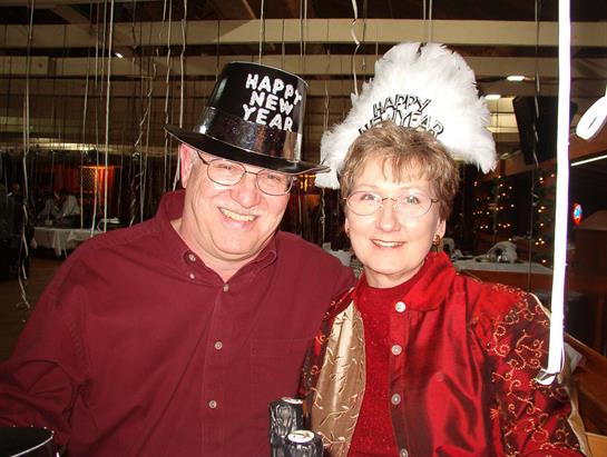 Joyful couple wears party hats and special outfits while celebrating New Year at a lively event.