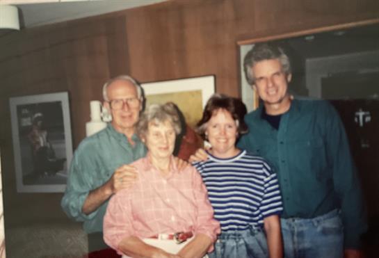 Four family members smile together in a warm, inviting living room, enjoying each other's company.