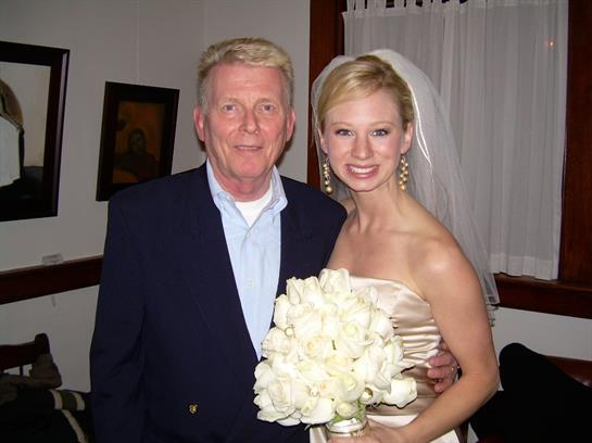 A bride in elegant attire stands with her grandfather, both smiling joyfully during the wedding.