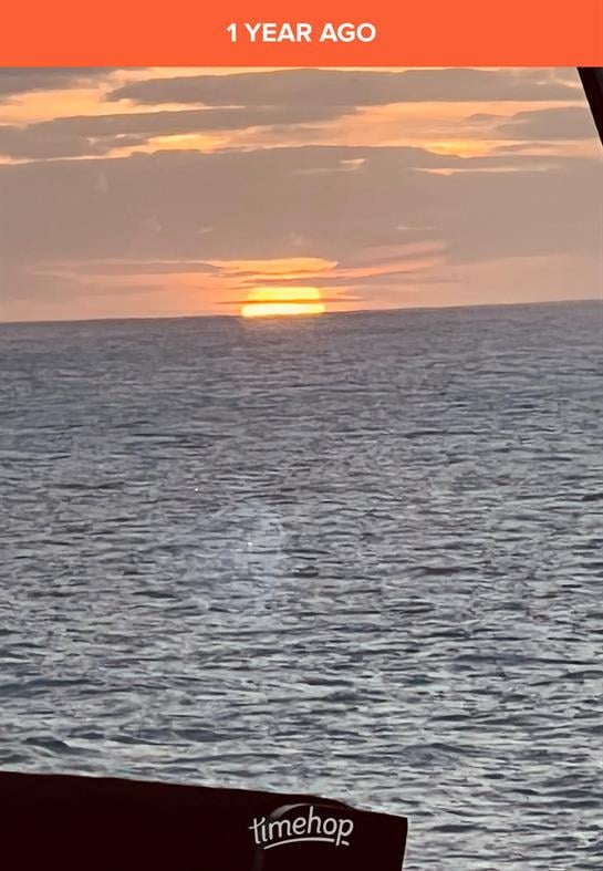 Golden sun setting gently behind the calm ocean, casting warm hues across the sky.