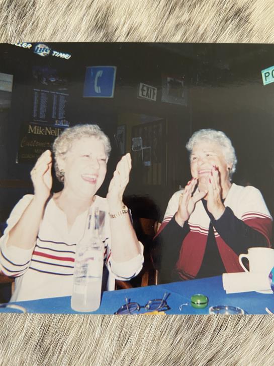 Two women smile and clap their hands while enjoying an entertaining moment together.