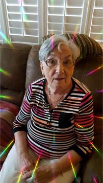 Senior woman smiles while seated on a couch surrounded by colorful light effects.