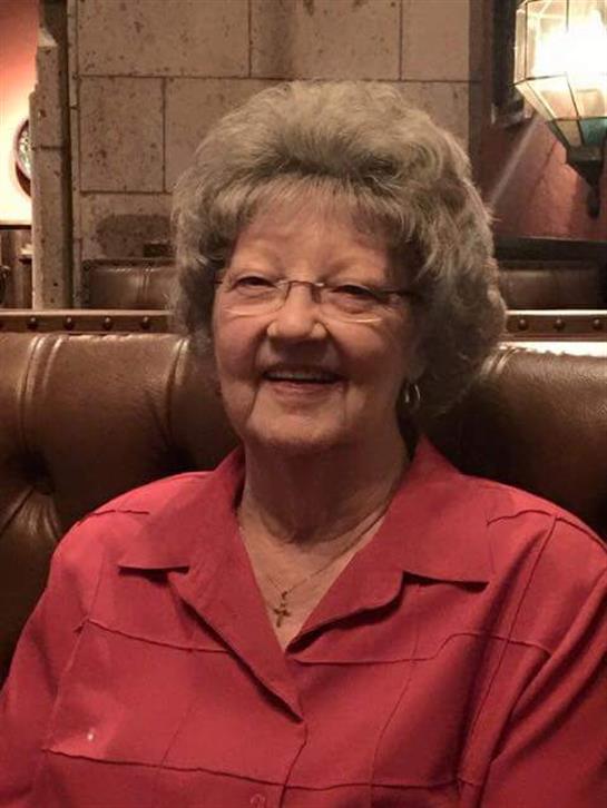 An elderly woman, dressed in red, sits comfortably smiling in a warm restaurant filled with decor.