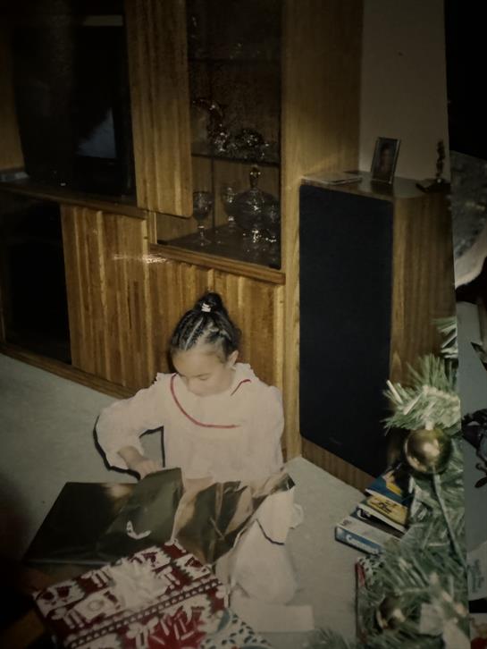 A girl unwraps presents with joy in a warmly decorated living room for Christmas.