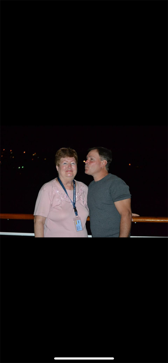 Two individuals share a joyful moment aboard a cruise ship at night, surrounded by city lights.