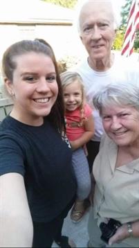 Four family members pose for a joyful selfie in a backyard on a sunny day.