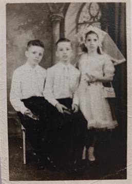 Three serious children in formal attire pose indoors, reminiscent of past celebrations.