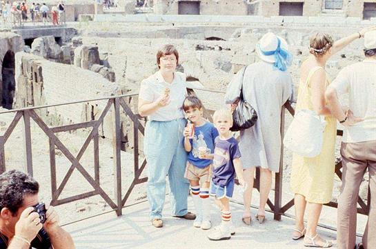 A family takes a memorable break with ice cream, surrounded by tourists at ancient ruins.
