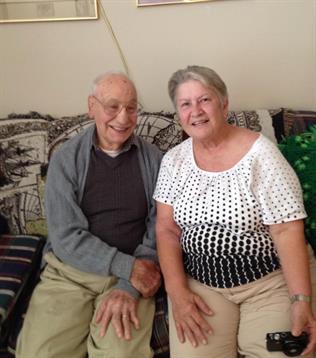 A happy elderly couple smiles while sitting close together on a patterned sofa at home.