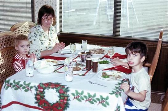 A woman and two children sit at a table covered in a holiday tablecloth, sharing a meal together.