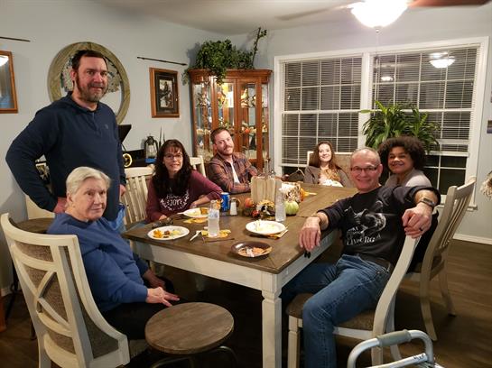A group of seven people sharing joyful moments over dinner in a warm, inviting space.