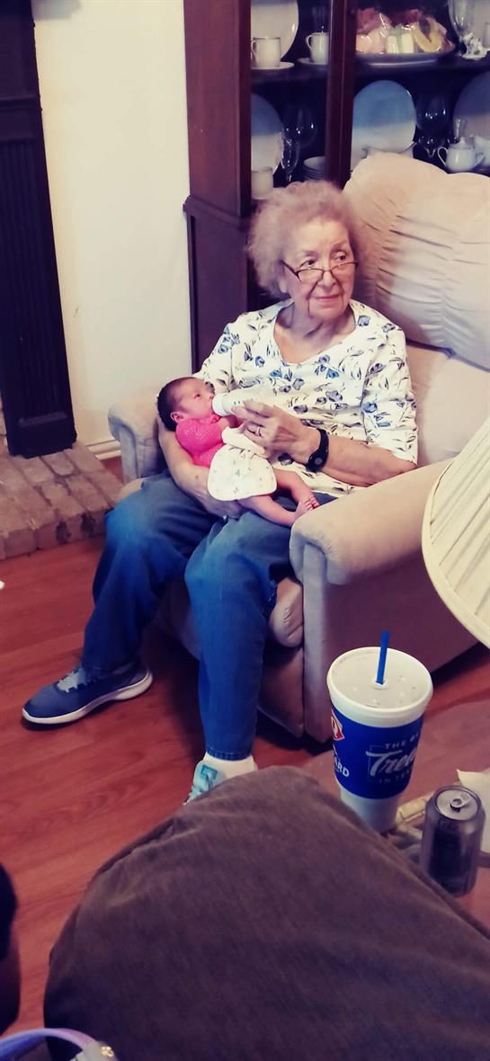 A grandmother sits in a cozy room, cradling her newborn granddaughter with affection.