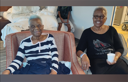 Two joyful elderly women are sitting on armchairs, enjoying time together in a hotel room.