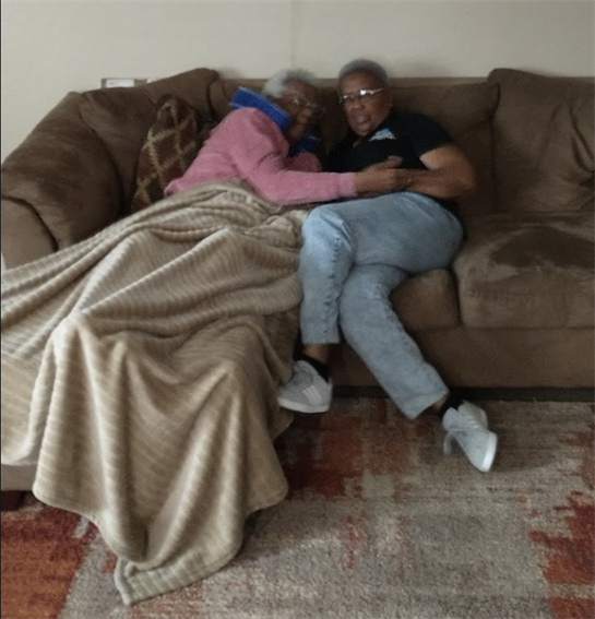 Two individuals are cuddled under a blanket on a couch, enjoying a peaceful moment together.