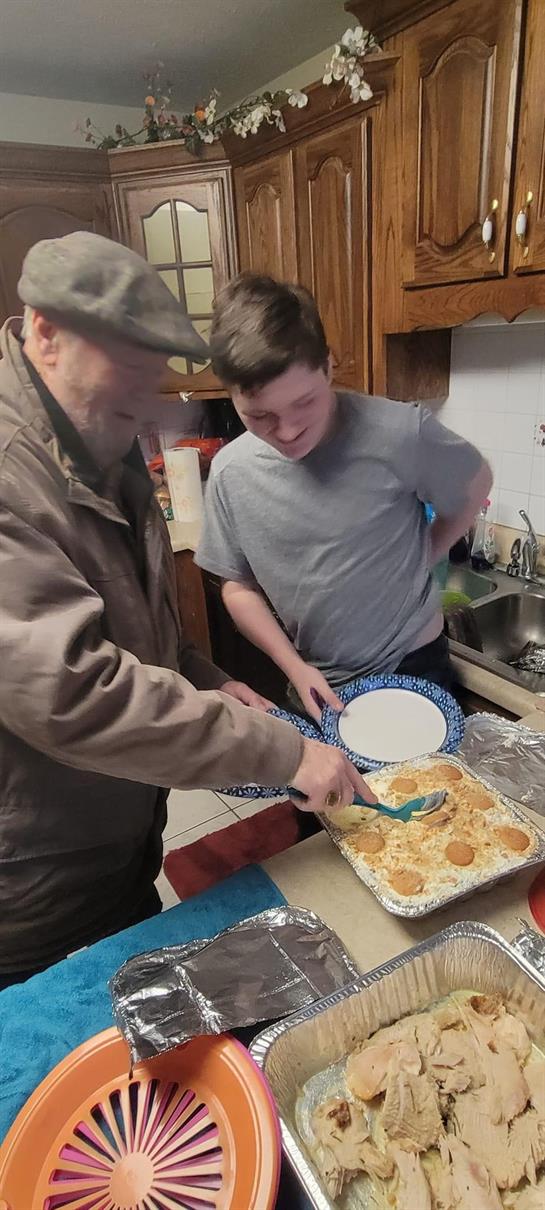 Grandfather and grandson happily serve a meal together in a cozy family kitchen.