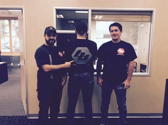 Three men in casual shirts proudly showcase their team's logo and camaraderie at work.