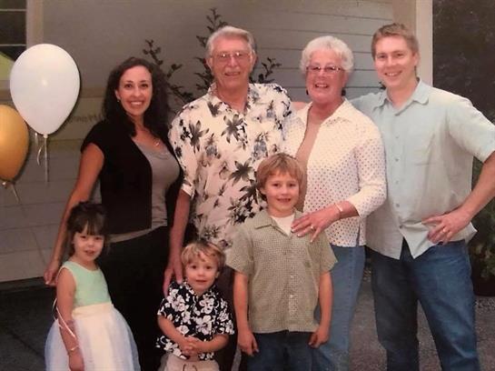 A group of family members smiles together outdoors, surrounded by balloons and greenery.