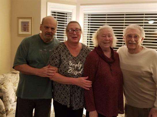 Four friends pose together in a warm living room with evening light filling the space.