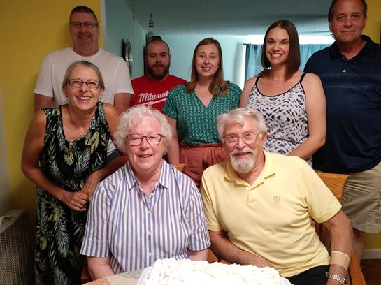 Family gathers around a big cake, smiling and celebrating joyfully together.