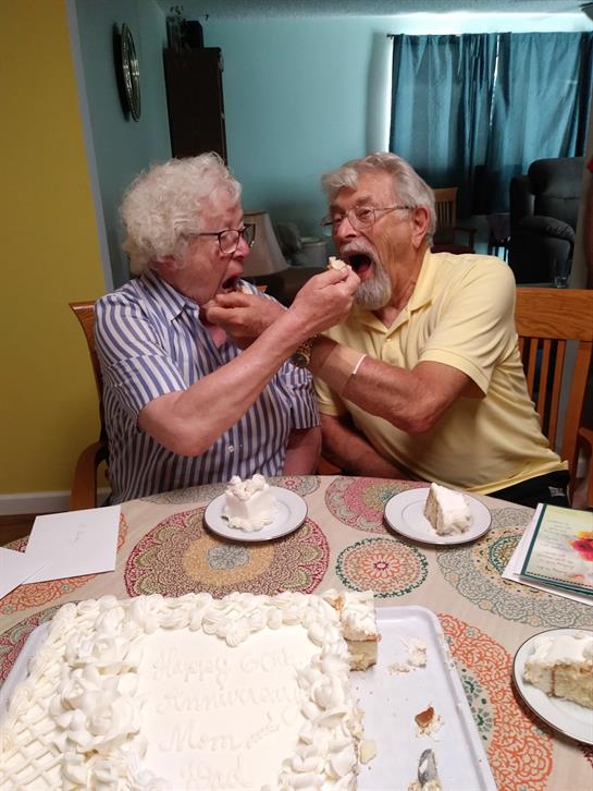 Two senior men share a fun moment feeding each other cake at a joyful celebration.