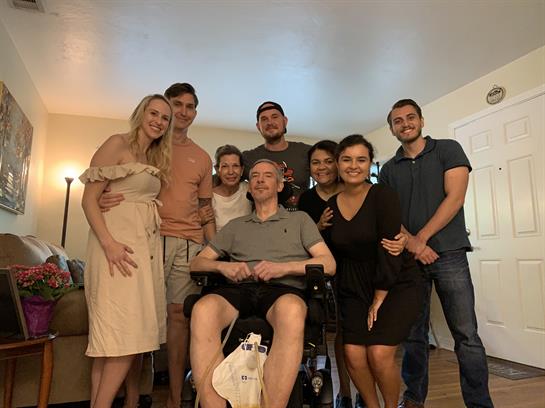 Group of friends and family members gather in a warm living room, sharing smiles and joy.